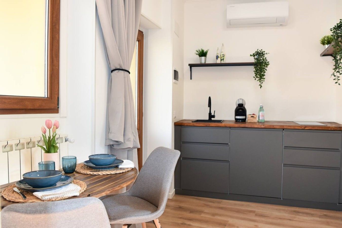 Eine moderne Küche mit grauen Schränken, einer Holz Arbeitsplatte und einem eingebauten Spülbecken. Es gibt einen Essbereich mit einem Tisch für zwei Personen, einem Stuhl und einer Vase mit Blumen.