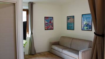 Ein Zimmer mit einer beigen Couch, einer Tür und drei gerahmten Postern an der Wand.