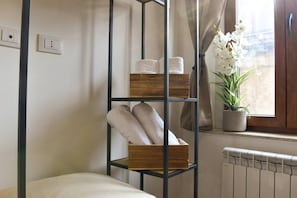 A room with a bed, a shelf with towels, a potted plant, and a window with curtains.