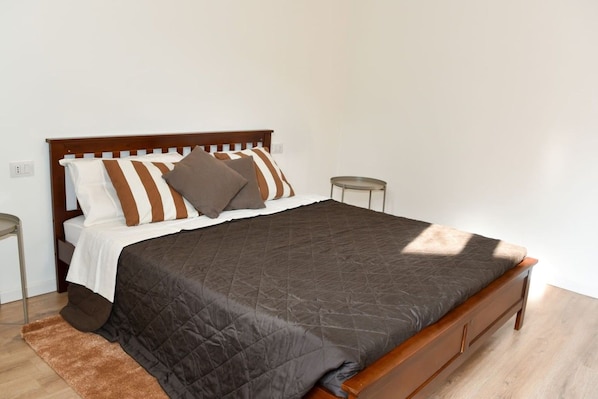 A single bed with a wooden headboard, a dark quilted bedspread, and two bedside tables with lamps.