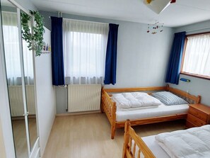 A bedroom with a wooden bed, a bedside table, a radiator, and a window with curtains. - Holiday Home With 2 Bedrooms (Sint Maartensvlotbrug)