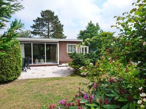 A modern house with a patio, a glass door entrance, and a garden with various plants and flowers. - Holiday Home With 2 Bedrooms (Sint Maartensvlotbrug)