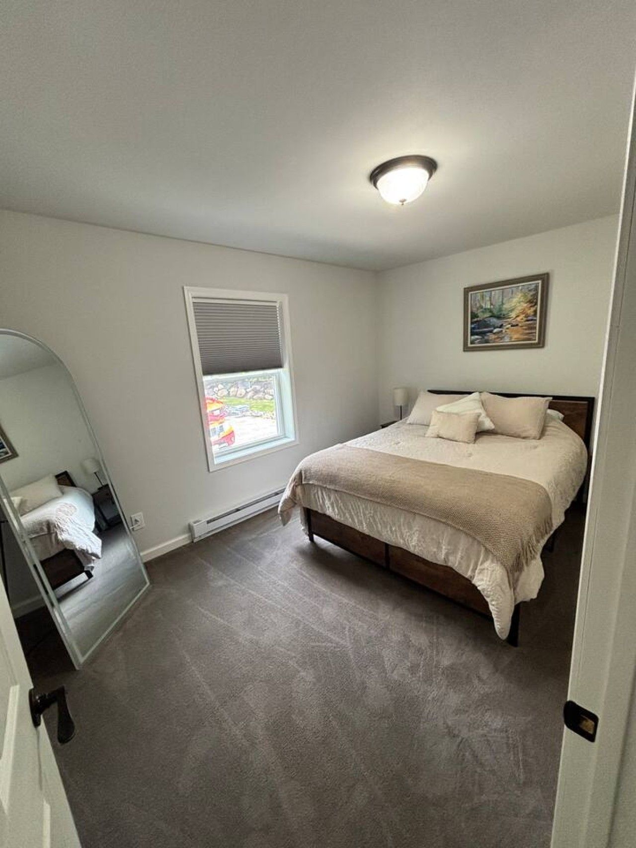 A bedroom with a bed, a window with blinds, a ceiling light, and a door.
