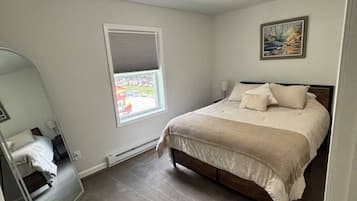 A bedroom with a bed, a window with blinds, a ceiling light, and a door.