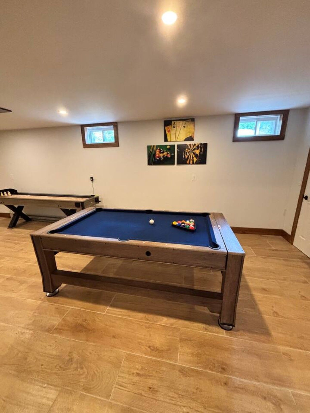 A pool table with balls, a dartboard, and two framed pictures on the wall.