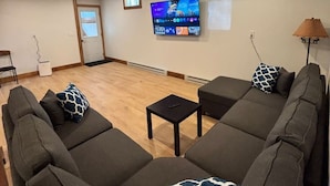 Un soggiorno con una grande TV a schermo piatto montata a parete, un divano, un tavolino e una lampada.