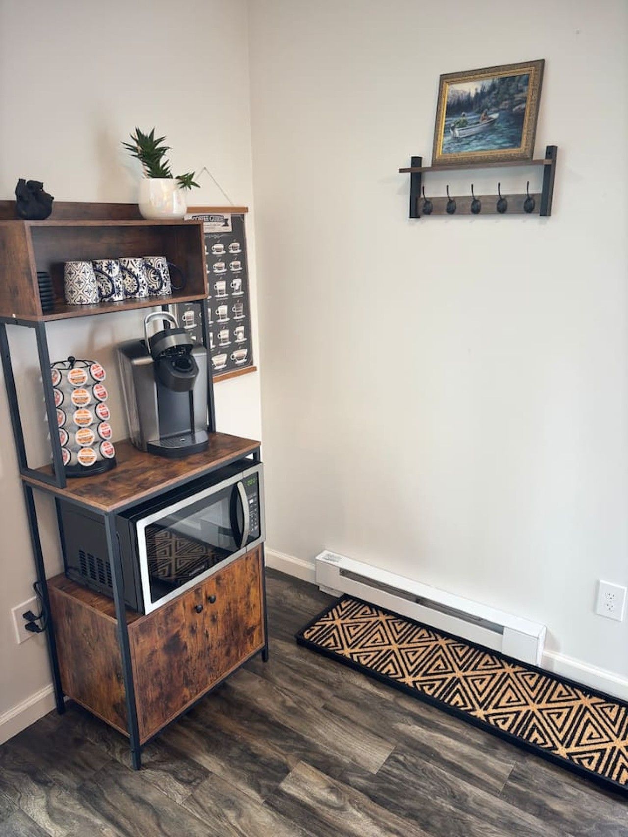 Una cocina equipada con cafetera, microondas y un armario. Hay una estantería con objetos decorativos y un cuadro en la pared.