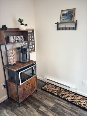 A kitchen area with a coffee machine, a microwave, and a cabinet. There is a shelf with decorative items and a framed picture on the wall. - The 48 Loon`s Landing (Lake Placid)