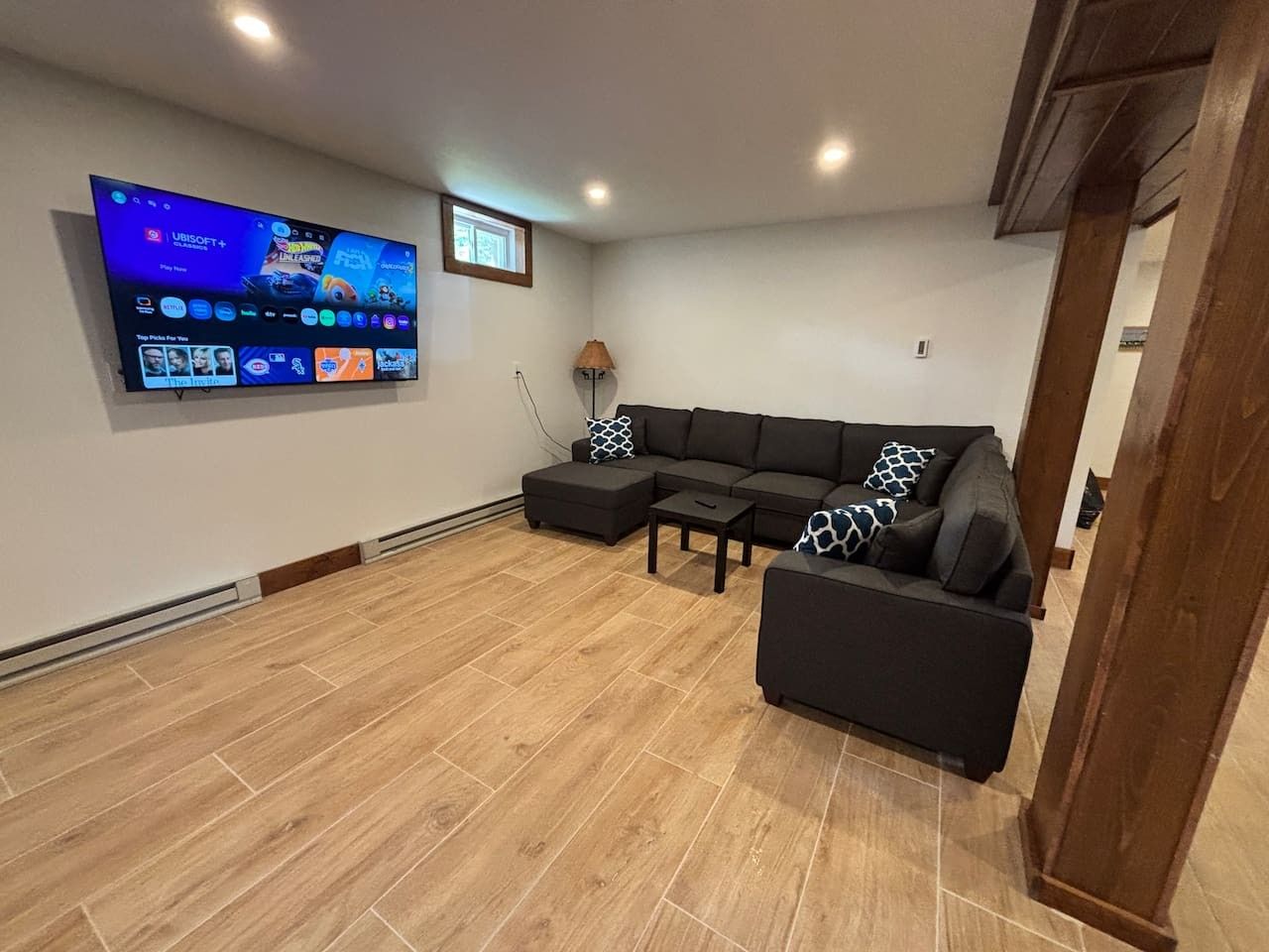 A living room with a flat-screen TV mounted on the wall, a sectional sofa, a coffee table, and a lamp.
