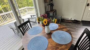 A wooden dining table with four blue placemats, surrounded by black chairs, in a room with a view of greenery through a glass door.