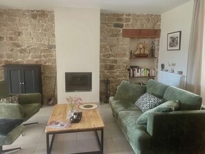 A living room with a stone wall, a fireplace, a green sofa, a wooden coffee table, and a bookshelf. - Michelle's House (Pont-l'Abbé)