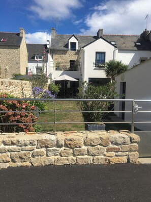 A stone wall with a metal gate, a white building with a balcony, and a clear blue sky. - Michelle's House (Pont-l'Abbé)