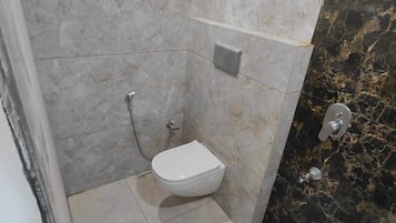 Un baño con inodoro, ducha y pared de mármol.