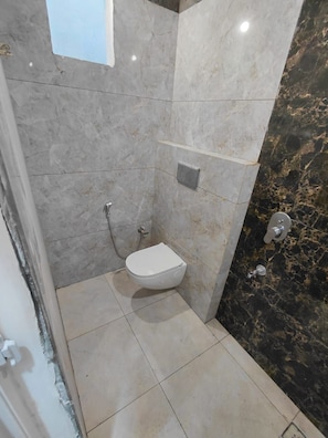 A bathroom with a toilet, a shower, and a marble wall. - Raj Tilak Guest House (Varanasi)