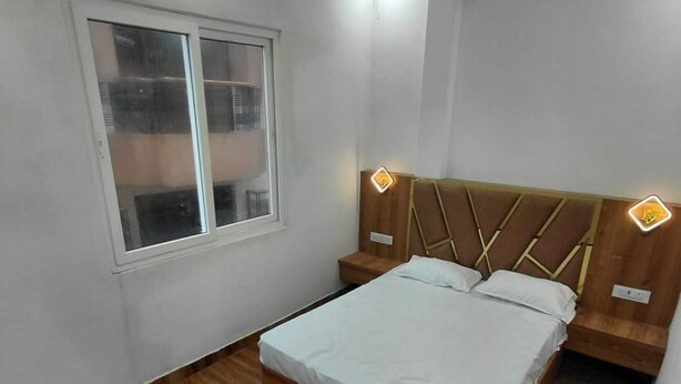 A bedroom with a wooden floor, a bed with a headboard, a window, and a ceiling fan. - Raj Tilak Guest House (Varanasi)