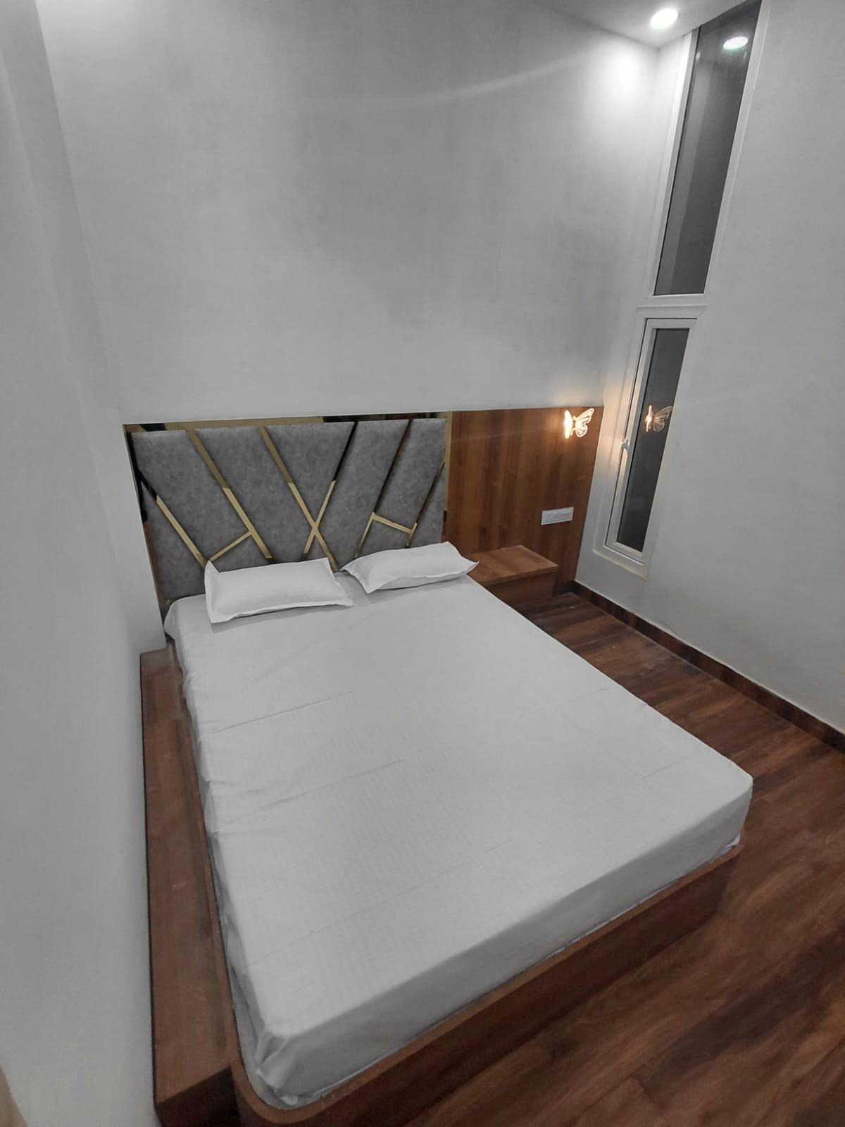 Ein Einzelbett mit Kopfteil in geometrischem Muster, ein Nachttisch mit Lampe sowie ein Fenster mit Blick ins Freie.