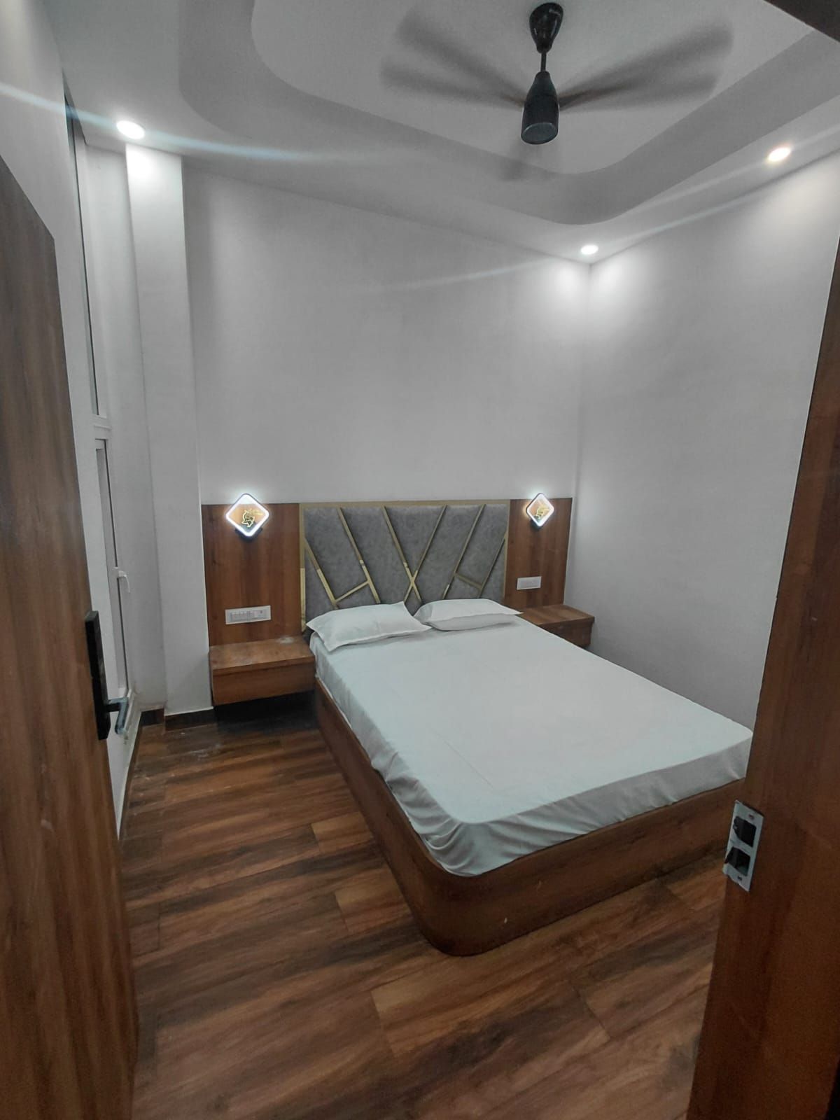 Ein modernes Schlafzimmer mit Bett, Holz-Kopfteil, Nachttischen und Deckenventilator.