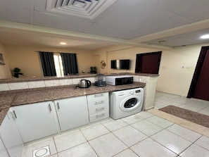 A compact kitchen with a washing machine, microwave, and cabinets. - Cozy 1-bedroom apartment in peaceful Dubai with AC (Dubai)