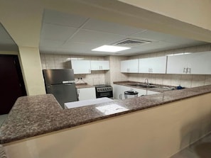 A kitchen with white cabinets, a granite countertop, a refrigerator, a stove, and a sink. - Cozy 1-bedroom apartment in peaceful Dubai with AC (Dubai)
