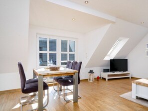 A modern loft-style room with a dining table, chairs, a television, and a skylight. - Holiday Apartment in Greetsiel With Balcony (Krummhoern)
