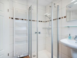 A modern bathroom with a glass-enclosed shower, a white radiator, and a sink with a mirror above it. - Holiday Apartment in Greetsiel With Balcony (Krummhoern)
