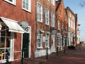 A row of traditional brick buildings with white window frames and awnings, likely commercial establishments. - Holiday Apartment in Greetsiel With Balcony (Krummhoern)