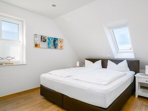 A bedroom with a large bed, a skylight, a wall art piece, and a window with blinds. - Holiday Apartment in Greetsiel With Balcony (Krummhoern)