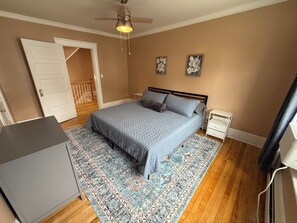 Ein Schlafzimmer mit Bett, Nachttischen, einem Schreibtisch, einem Deckenventilator und einer Tür zu einer Treppe.