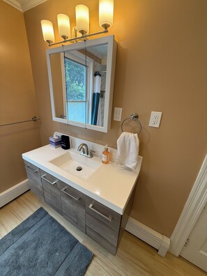 A bathroom with a large mirror, a white sink, a towel rack, and a window with curtains. - Dog-Friendly 3BR Townhome · Parking & Workspace (Southbridge)