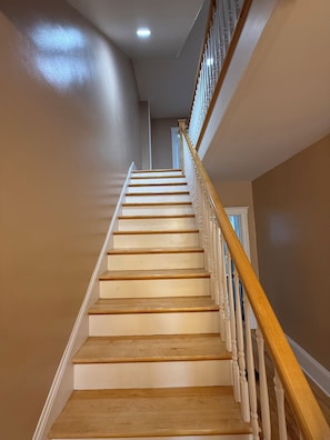 A staircase with wooden steps and white handrails, leading to a landing with a door. - Dog-Friendly 3BR Townhome · Parking & Workspace (Southbridge)