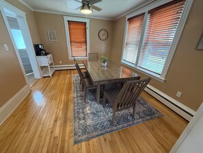 A dining area with a wooden table, chairs, a clock, and two windows with blinds. - Dog-Friendly 3BR Townhome · Parking & Workspace (Southbridge)