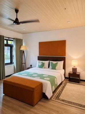 A hotel room with a bed, a standing lamp, a ceiling fan, and a window with curtains.