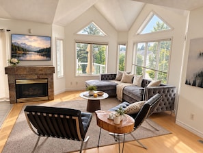 A modern living room with a fireplace, large windows, a sectional sofa, and a coffee table. - Waterfront ski retreat on Blue Mountain. Pet-Friendly! (Collingwood)