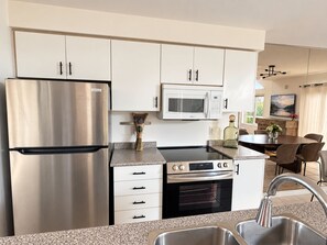 Una cocina moderna con electrodomésticos de acero inoxidable, gabinetes blancos, horno empotrado y encimera de granito.