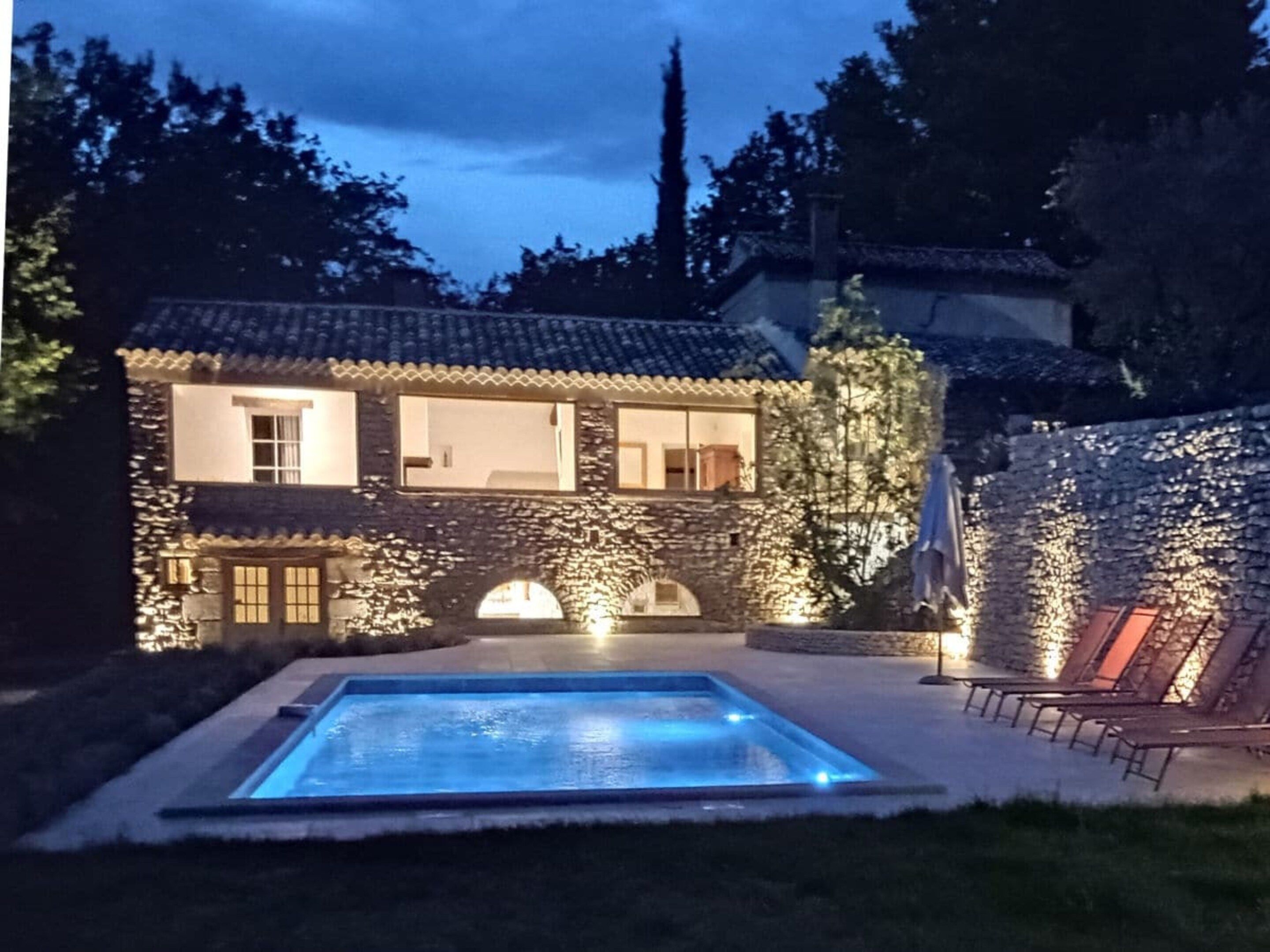 A house with a swimming pool, stone walls, and a tiled roof.