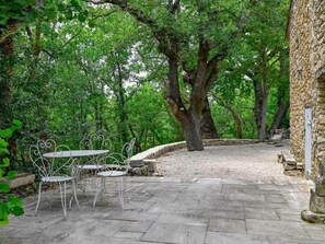An outdoor patio with stone flooring, surrounded by trees and a stone wall. - Domaine de la Santonne (Apt)