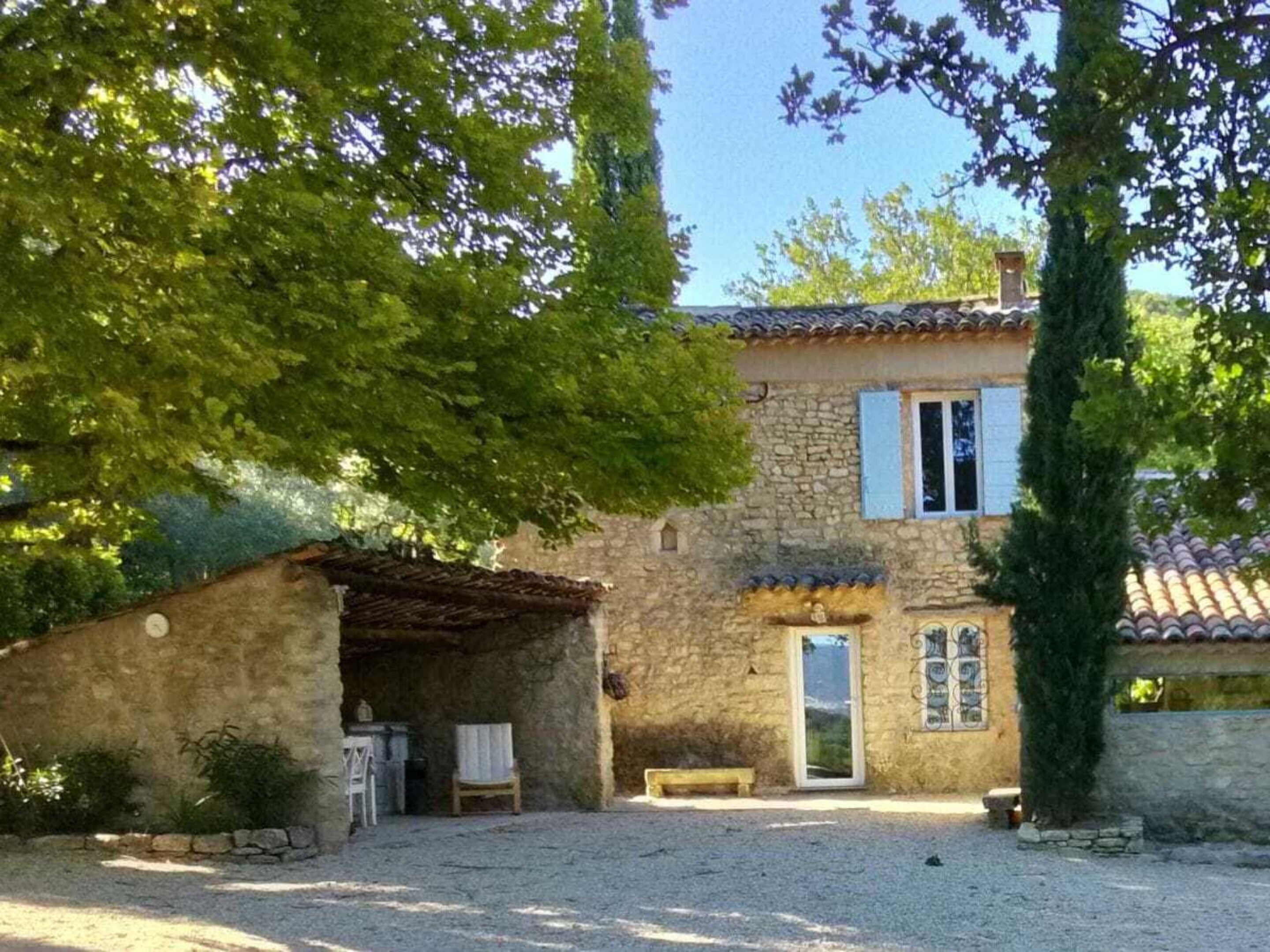 A stone building with a tiled roof, a covered porch, and a small garden area.