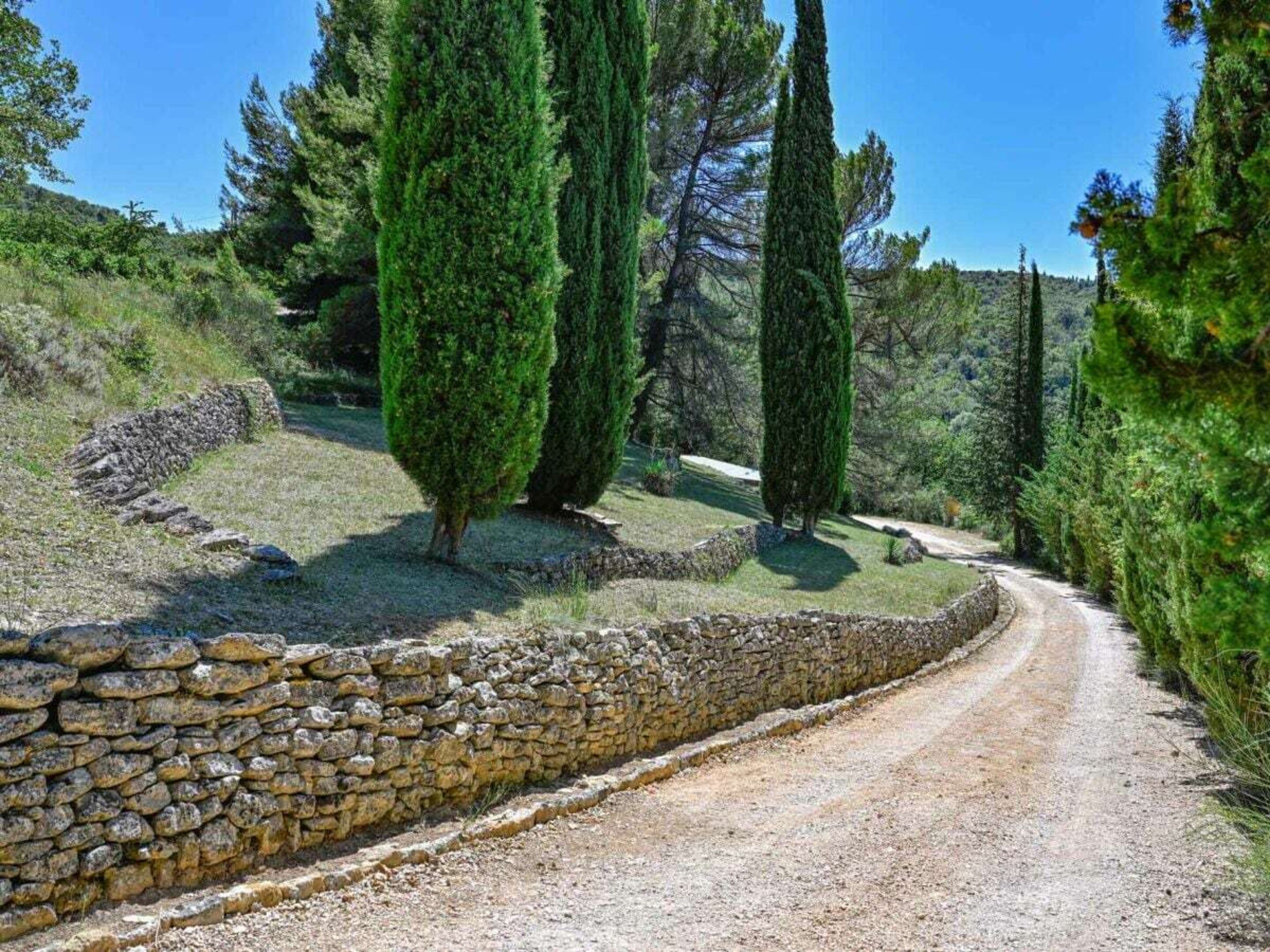 A gravel path flanked by stone walls and tall cypress trees.