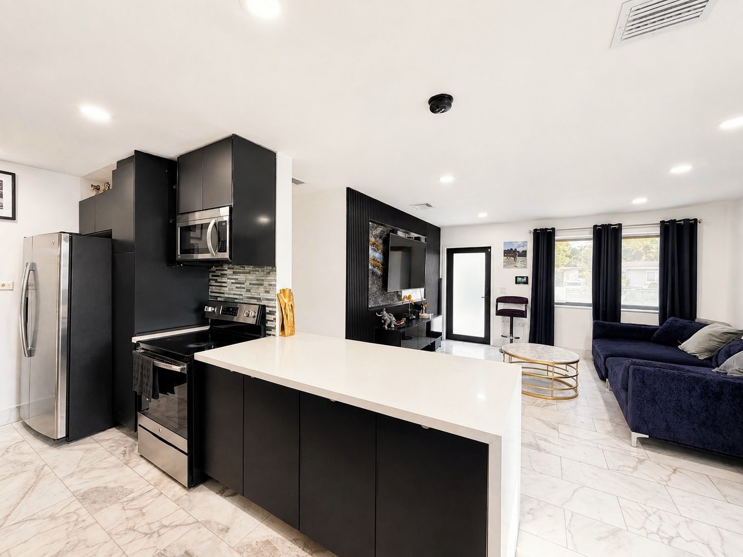 A modern kitchen with a central island, built-in appliances, and a dining area with a sofa and table.