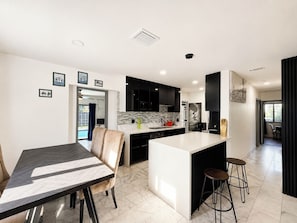 A modern kitchen with black cabinets, a white island, and a dining area with a table and chairs. - ★★★★★ Casa Celeste - Chic and Serene Miami Villa (Miami)