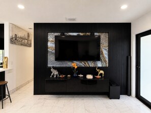 A modern living room with a large flat-screen TV mounted on a black wall with a marble-like texture. - ★★★★★ Casa Celeste - Chic and Serene Miami Villa (Miami)