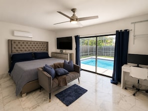 A bedroom with a bed, a TV, a desk, and a view of a swimming pool. - ★★★★★ Casa Celeste - Chic and Serene Miami Villa (Miami)