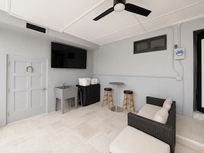 A modern room with a ceiling fan, a flat-screen TV, a sink, stools, and a sofa. - ★★★★★ Casa Celeste - Chic and Serene Miami Villa (Miami)