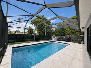 En swimmingpool med en klar blå vandoverflade, omgivet af en overdækket patio med en metaldækket konstruktion.