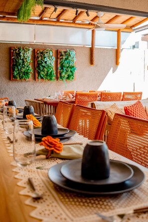 A restaurant setting with tables set for dining, featuring woven chairs and a ceiling fan. - Casa Linda a poucos passos do mar (Sao Miguel dos Milagres)