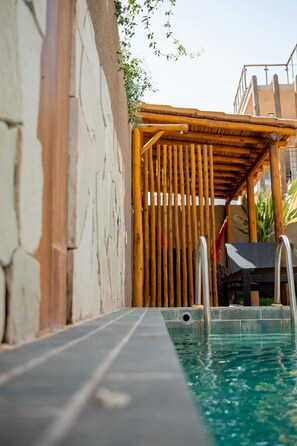 A pool area with a bamboo fence, a stone wall, and a clear view of the water. - Casa Linda a poucos passos do mar (Sao Miguel dos Milagres)