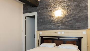 Une chambre d’hôtel avec un lit, une tête de lit en bois, un mur en pierre et un luminaire.
