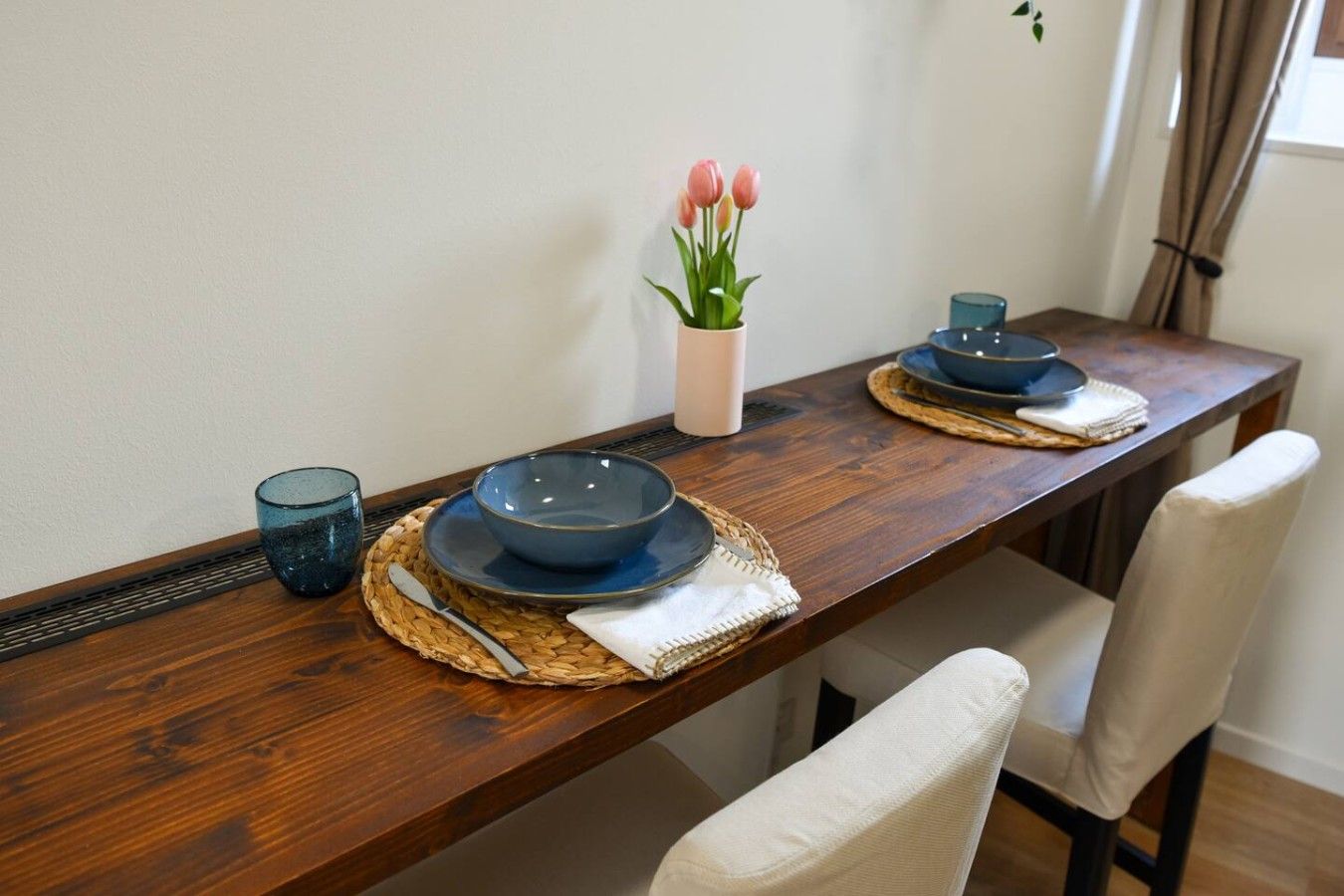 Une table à manger en bois, avec des assiettes bleues, un verre et un vase rempli de fleurs.