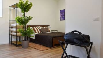 A bedroom with a bed, a potted plant, a suitcase, and a wall-mounted shelf.