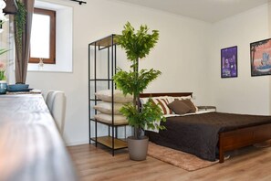 A bedroom with a bed, a bedside table, a potted plant, a window, and wall art. - Fly&Rest MXP | Suite | Airport Transfer 24/7 (Casorate Sempione)